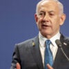 Israeli Prime Minister Benjamin Netanyahu, wearing a suite and blue tie, speaks into a microphone.