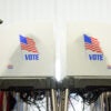 An older male and female vote in face-to-face-voting booths.
