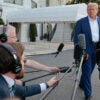 Donald Trump strolls past a group of reporters all pointing microphones at him.