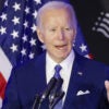 Former President Joe Biden at a microphone with a U.S. flag behind him