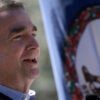 Ralph Northam speaking outdoors with a Virginia flag in the background