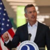 Transportation Secretary Sean Duffy in a suit with no tie gestures with his right hand while speaking at a podium.